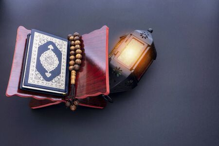 Holy Al Quran with written arabic calligraphy meaning of Al Quran, lantern lamp and rosary beads or tasbih on black background.の写真素材