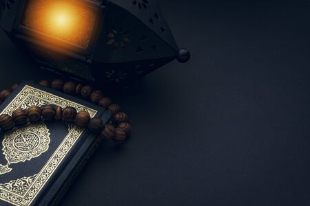 Holy Al Quran with written arabic calligraphy meaning of Al Quran and rosary beads or tasbih on black background. Copy space and crop fragmentの写真素材