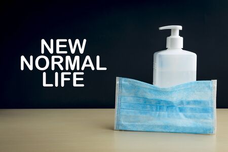 NEW NORMAL LIFE text with face mask and hand sanitizer on wooden background. Covid 19 and coronavirus conceptの写真素材