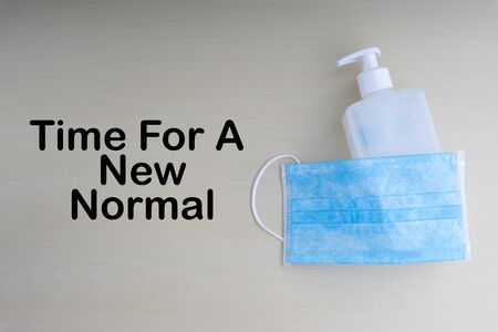 TIME FOR A NEW NORMAL text with face mask and hand sanitizer on wooden background. Covid 19 and coronavirus conceptの写真素材