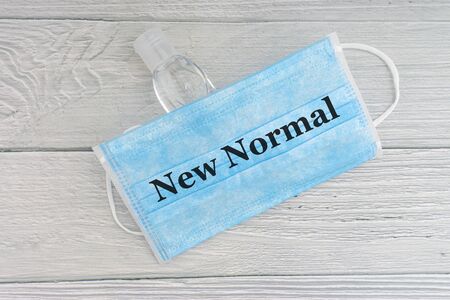 NEW NORMAL text with face mask and hand sanitizer on wooden background. Covid 19 and coronavirus conceptの写真素材