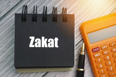 ZAKAT or ISLAMIC TAX  text with fountain pen, calculator and notepad on wooden background. Zakat is a form of alms-giving treated in Islam as a religious obligation or tax. Business and islamic conceptの写真素材