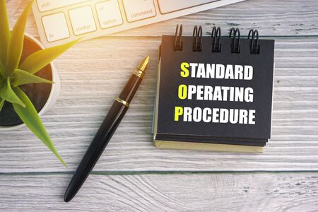 STANDARD OPERATING PROCEDURE text with fountain pen, decorative plant, keyboard and notepad on wooden background. Business conceptの写真素材