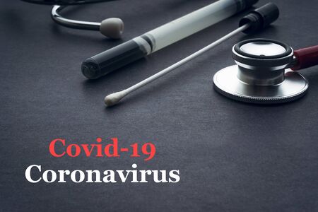 COVID-19 or CORONAVIRUS text with stethoscope and medical swab on black background. Covid-19 or Coronavirus concept.の写真素材
