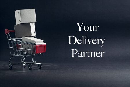 YOUR DELIVERY PARTNER text with shopping cart on dark background. Business, Copy space and online shopping concept. Selective focusの写真素材