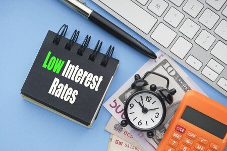 LOW INTEREST RATES text with keyboard, fountain pen, alarm clock, banknotes currencies and calculator on blue background.Coronavirus Covid19 and Business Conceptの写真素材