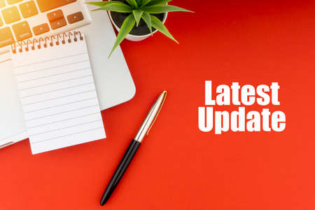 LATEST UPDATE text with notepad, laptop, fountain pen and decorative plant on red background. Business and Copy Space Conceptの写真素材