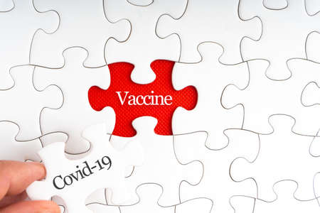 COVID-19 VACCINE text with jigsaw puzzle on red background. Covid-19 and Coronavirus Conceptの写真素材