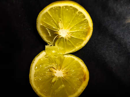 A yellow ripe lemon is cut in the middle and contains seeds and lemon juice. It is placed on a black background.の写真素材