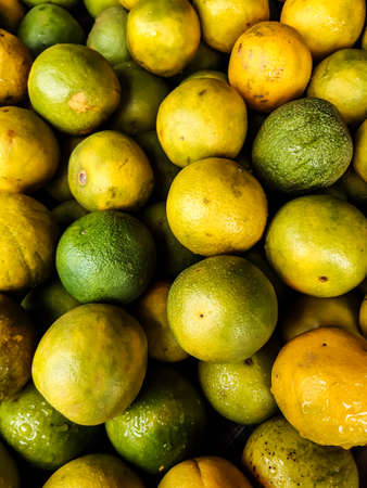 Ripe yellow and green seasonal lemons are many together in a basket in front of a store. This fruit is very tasty and sweet.の写真素材