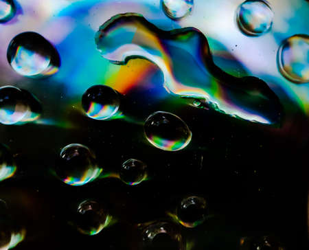 Drops of rain water are falling on CD dix and reflecting. Yellow-blue and red light is being reflected.の写真素材