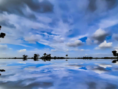 At sunset, farmland in Indian villages and black clouds in the blue sky, through which the light of the sun is shining.の写真素材