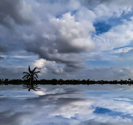 At sunset, the village environment of India, the blue sky reflects the black and white clouds and the water reflects the shadows of the clouds.の写真素材