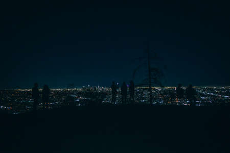 Nighttime view of people against the Los Angeles skyline.