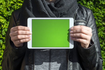 woman holding white tablet with green blank display in her hands in a parkの写真素材
