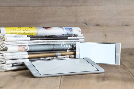Empty screens of tablet and smartphone and variety of newspaper issues with wood in background