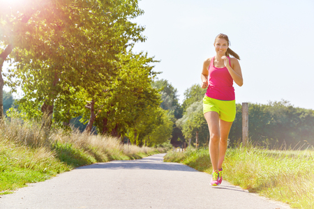 Young woman running smiling along pathの写真素材