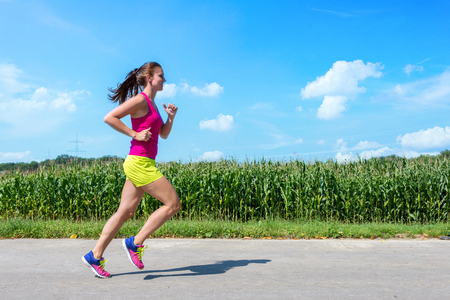 Sporty woman running along corn field during sunny dayの写真素材