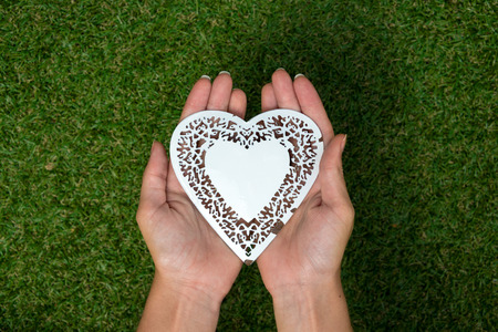 White metal heart placed in two hands held above meadowの写真素材
