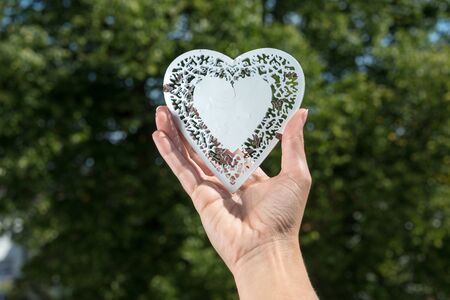 White metal heart held in hand in a park during summer as a closeup viewの写真素材