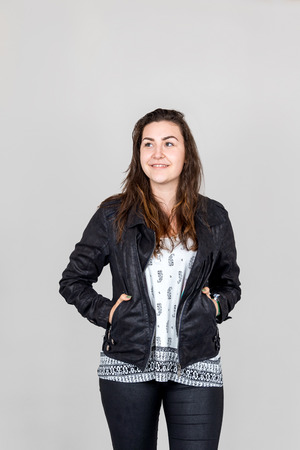 Studio shot of smiling woman looking into the camera with hands in her pockets of leather jacketの写真素材