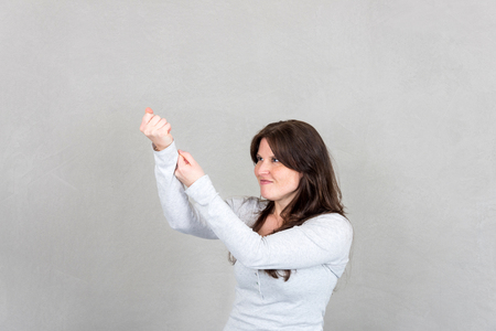 Studio shot of young woman pulling an imaginary rope with both handsの写真素材