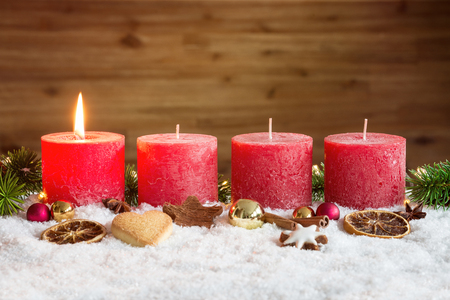 Four red advent candles with first candle lit and christmas decoration lying in snow as templateの写真素材