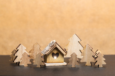 Carved wooden fir trees and wooden cottage with heart  in front of brown background as templateの写真素材