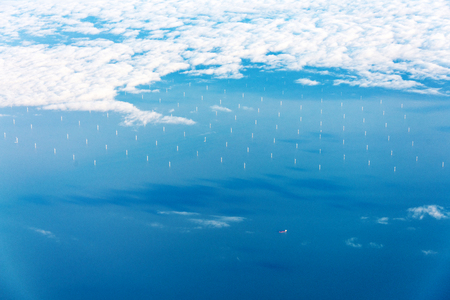 Offshore wind farm from above in blue water and with white clouds at horizon