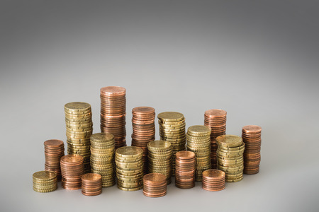 Different stacks of euro coins in front of grey background symbolizing savings