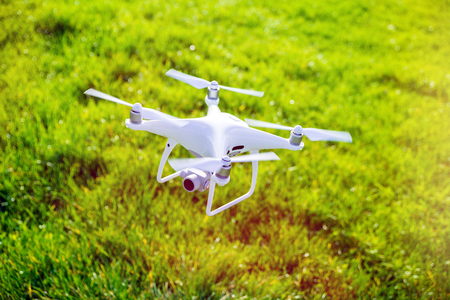 Flying white professional quadcopter drone camera with green grass in backgroundの写真素材