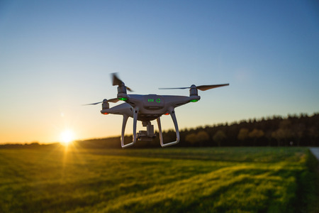 Flying white professional quadcopter drone camera during sunset