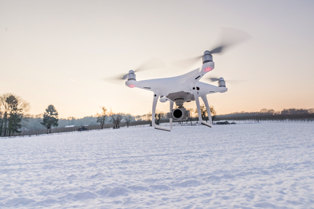 Photo of a flying white professional quadcopter drone camera in the air with white snow in winter in...
