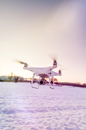 Photo of a flying white professional quadcopter drone camera in the air with white snow in winter in front of forestの写真素材