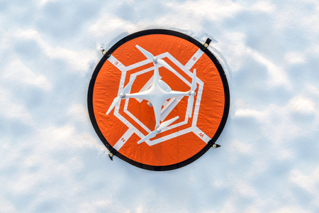 Photo of a white professional quadcopter drone camera standing on heliport with white snow in winter の写真素材