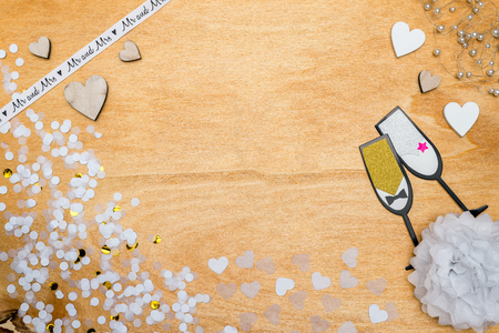Wedding decoration for party with white and gold confetti, champagne glasses and wooden hearts lying on wooden background as flatlayの写真素材