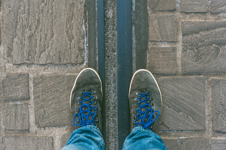 Reaching a crossroads having to decide about past, now and future symbolized by two feet and shoes standing on two different colors on pathway from aboveの写真素材