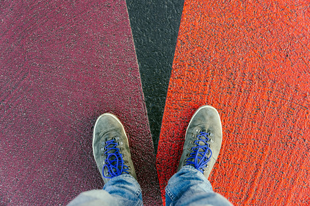 Reaching a crossroads having to decide about past, now and future symbolized by two feet and shoes standing on two different colors on pathway from aboveの写真素材