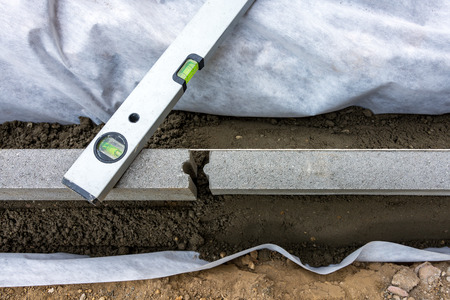 Setting edge restraints buy putting border curb stones in earth-moist concrete with bubble level