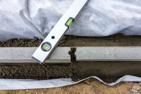 Setting edge restraints buy putting border curb stones in earth-moist concrete with bubble levelの写真素材