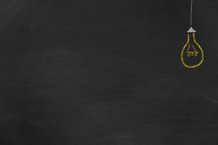 Yellow light bulb painted with chalk on dirty black chalkboard in school with free copy spaceの写真素材