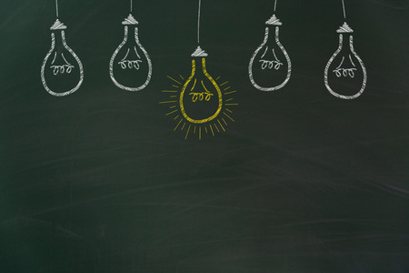 Yellow and white light bulbs painted with chalk on dirty green chalkboard with free copy spaceの写真素材