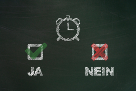 Yes and no written in german with chalk and painted checkboxes with clock on green chalkboard symbolizing the european union survey concerning the summertime arrangementsの写真素材