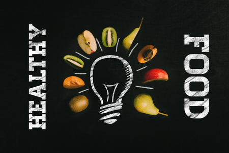 Healthy food written with chalk in white with light bulb painted on black chalkboard surrounded by fresh healthy cut fruits as templateの写真素材
