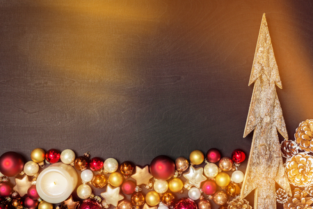 Christmas baubles decoration and wooden fir tree as frame with grey candle against black background as flatlay from aboveの写真素材