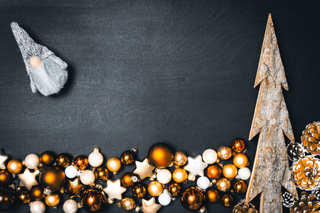 Christmas baubles decoration and wooden fir tree as frame with grey christmas elf for happy new year message against black background as flatlay from aboveの写真素材