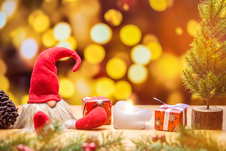 Sitting christmas elf with bokeh lights in background surrounded by christmas decorations as tree and gift boxesの写真素材