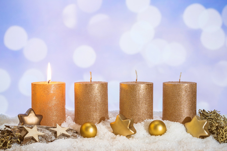 Four golden advent candles with first candle lit and christmas decoration lying in snow as templateの写真素材