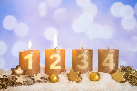 Four numbered gold advent candles with two candles lit and christmas decoration lying in snow as templateの写真素材