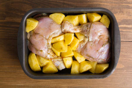 Raw chicken and potatoes with spice on wooden background